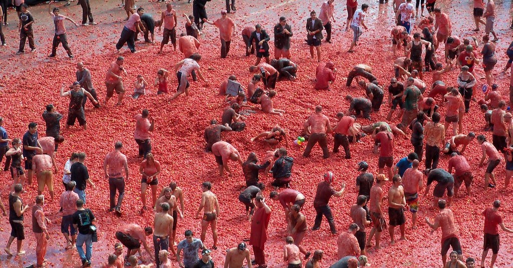 Participants at the La Tomatina festival in Buñol, Spain, joyfully throwing tomatoes in the streets, creating a vibrant scene filled with red pulp.